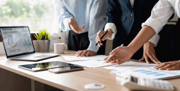 Business professionals collaborating around a conference table reviewing charts and data reports on paper and laptop screen, illustrating the collaborative assessment process used in business process reviews and software usage assessments for construction companies