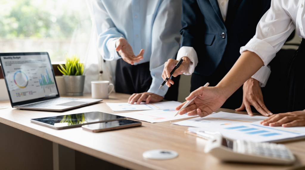 Business professionals collaborating around a conference table reviewing charts and data reports on paper and laptop screen, illustrating the collaborative assessment process used in business process reviews and software usage assessments for construction companies