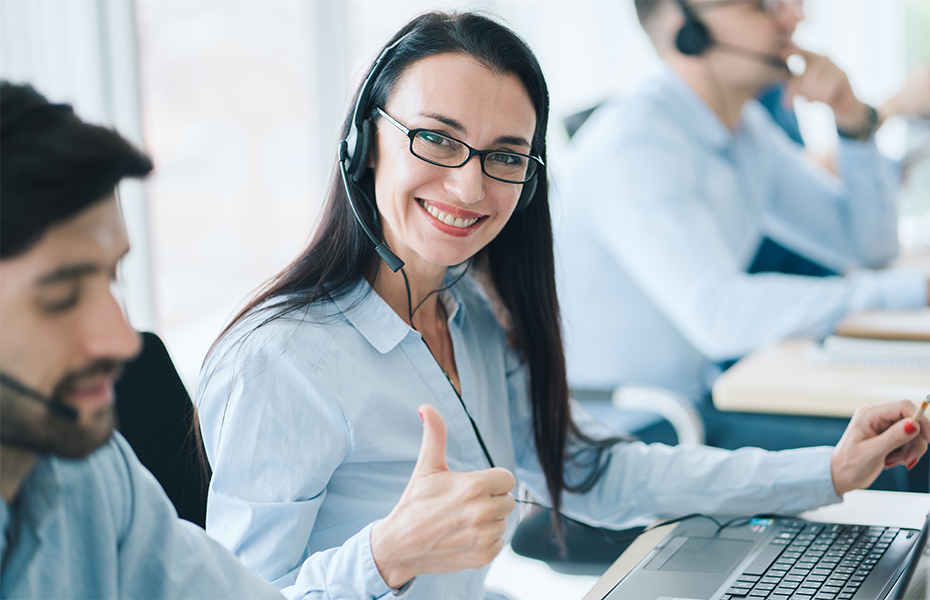 Help desk technician on computer with headset giving thumbs up