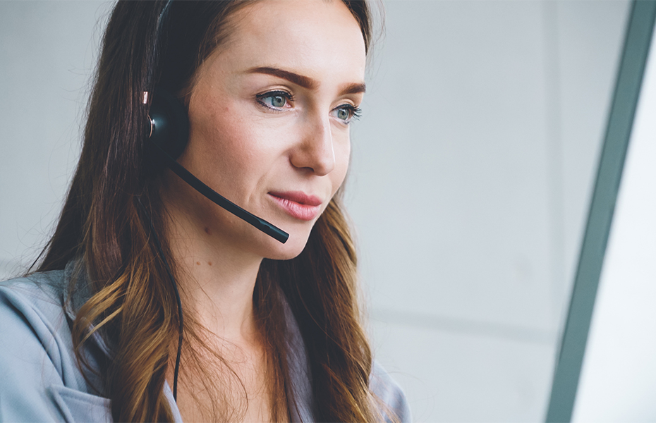 A woman looking at a computer screen and wearing a headset.