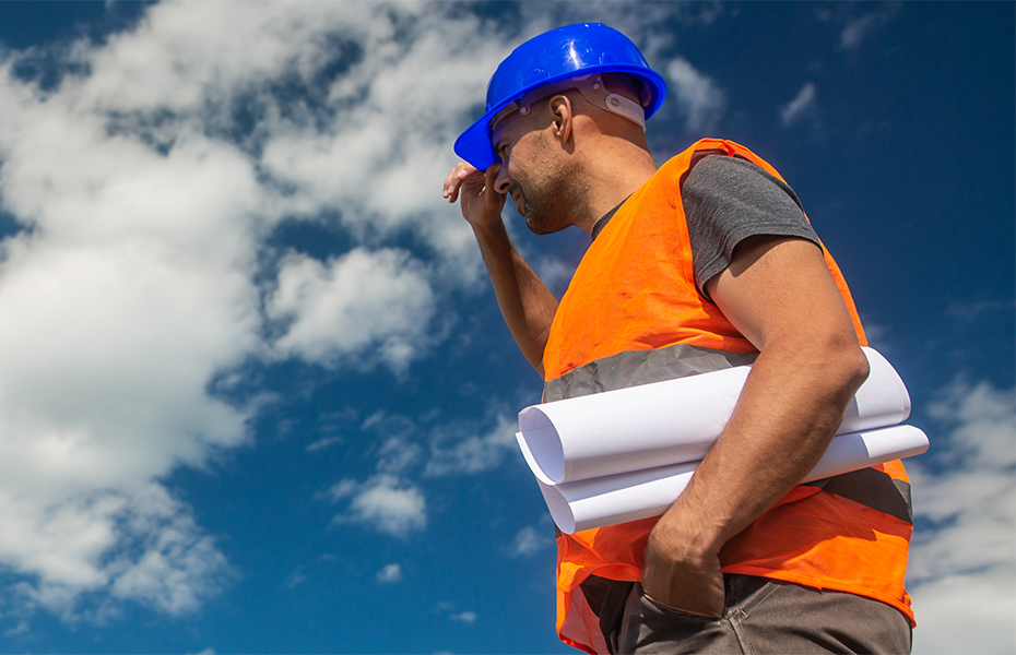 A construction worker holding a rolled piece of paper and looking to the left.