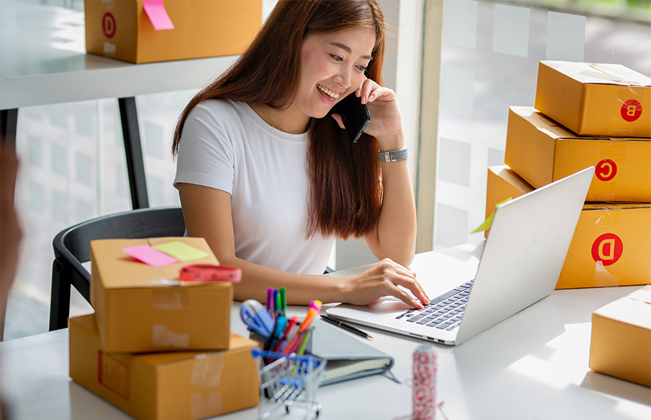 A young woman working on a laptop while talking on a cellphone.