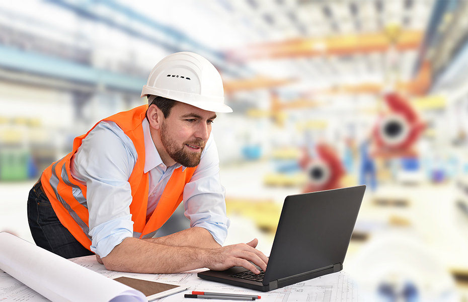 A man in a hardhat working at a laptop.