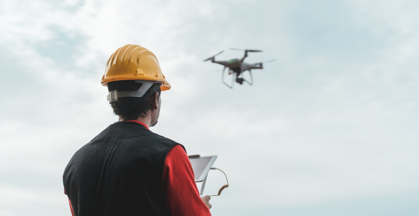 Man on construction jobsite in a yellow hard hat working with a drone.