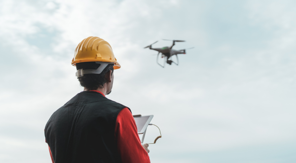 Man on construction jobsite in a yellow hard hat working with a drone.